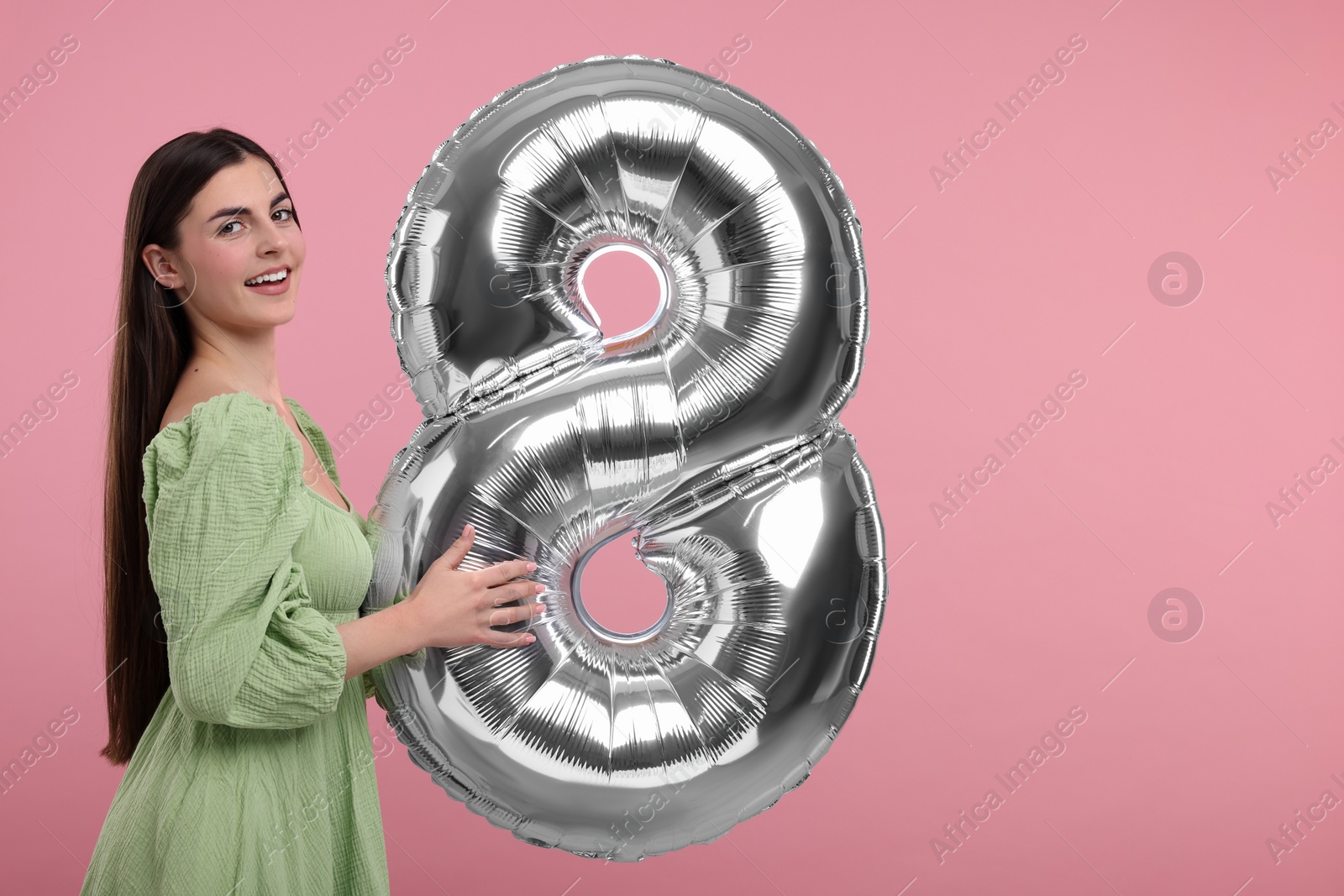 Photo of Happy Women's Day. Charming lady holding balloon in shape of number 8 on dusty pink background, space for text