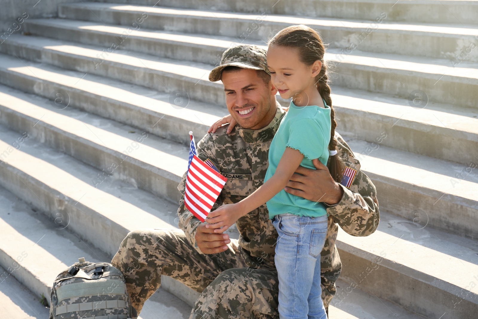 Photo of Soldier and his little daughter with flag of USA outdoors, space for text