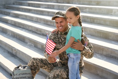Soldier and his little daughter with flag of USA outdoors, space for text