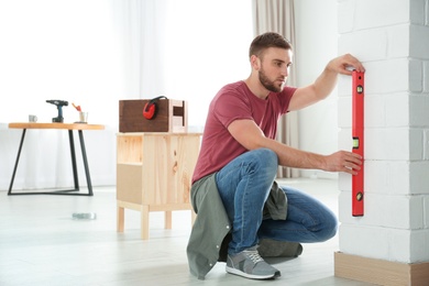 Photo of Young working man using construction level at home, space for text