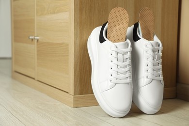Photo of Orthopedic insoles in shoes near wooden drawer, space for text
