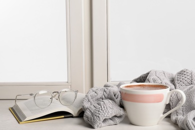 Photo of Composition with cup of hot chocolate and book on windowsill, space for text. Winter drink