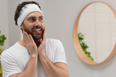 Washing face. Man with headband in bathroom, space for text