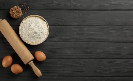 Flat lay composition with wheat flour and eggs on black wooden table. Space for text