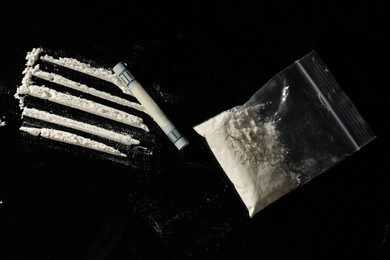Photo of Drug addiction. Plastic bag with cocaine and rolled dollar banknote on black background,, flat lay