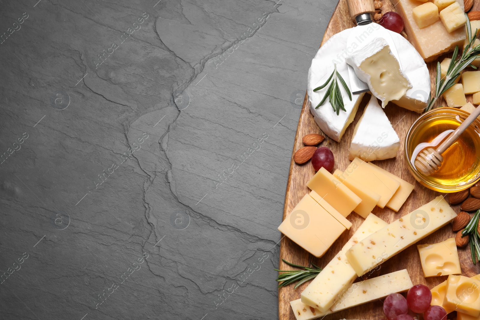 Photo of Cheese plate with honey, grapes and nuts on black table, top view. Space for text