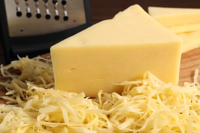 Photo of Grated and whole piece of cheese on wooden board, closeup