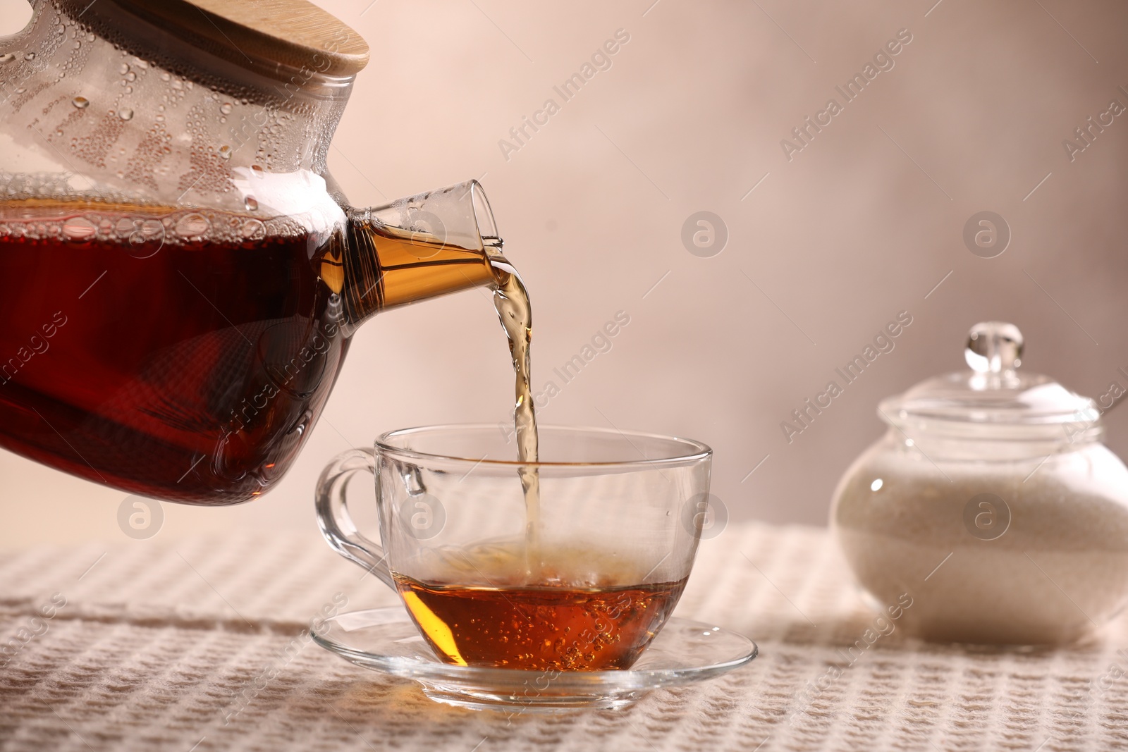 Photo of Pouring aromatic tea into cup at table, closeup