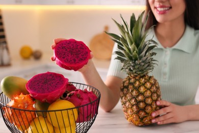 Young woman with fresh exotic fruits at table indoors, closeup
