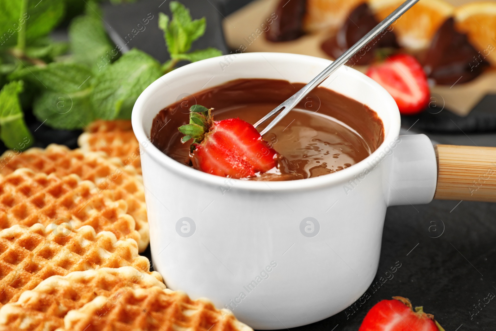 Photo of Dipping strawberry into fondue pot with milk chocolate on table, closeup