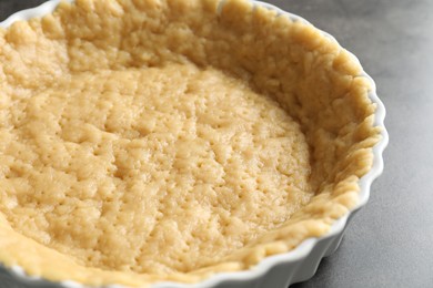 Making shortcrust pastry. Raw dough in baking dish on grey table, closeup