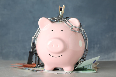 Piggy bank with steel chain, padlock and banknotes on grey marble table. Money safety concept