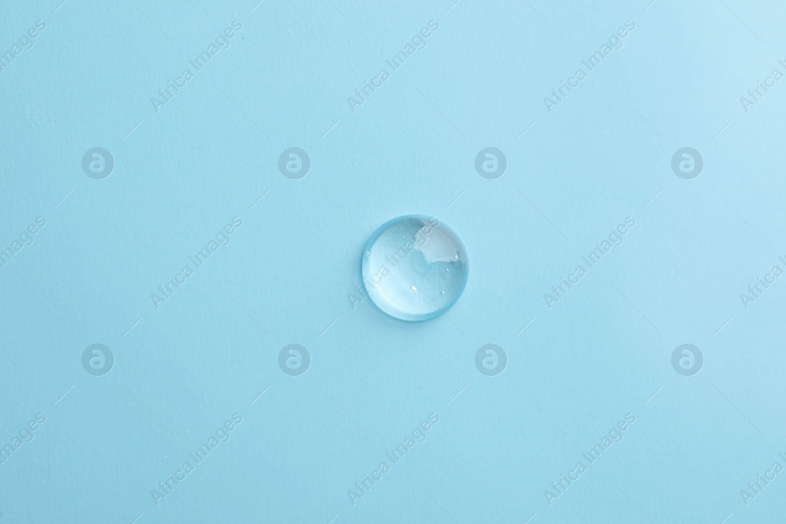 Photo of Drop of transparent ointment on light blue background, top view