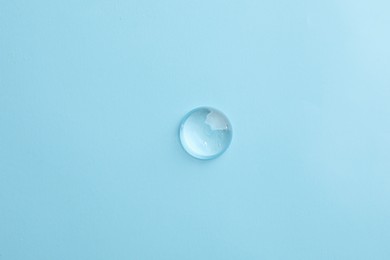 Photo of Drop of transparent ointment on light blue background, top view