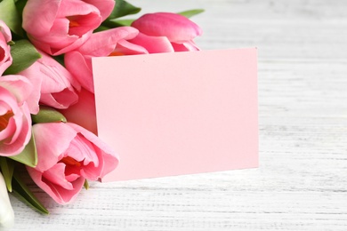 Photo of Beautiful spring tulips and card on light wooden background, space for text. International Women's Day