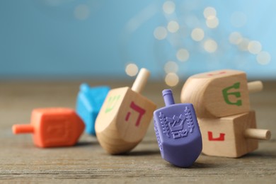 Photo of Hanukkah celebration. Dreidels with jewish letters on wooden table against light blue background with blurred lights, closeup. Space for text