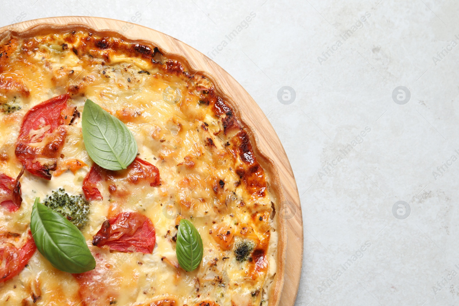 Photo of Tasty quiche with cheese, tomatoes and basil leaves on light grey table, top view. Space for text