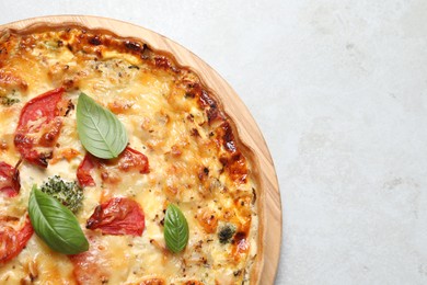 Photo of Tasty quiche with cheese, tomatoes and basil leaves on light grey table, top view. Space for text