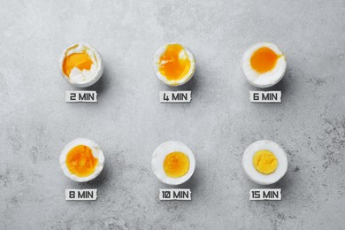 Different readiness stages of boiled chicken eggs on light grey table, flat lay