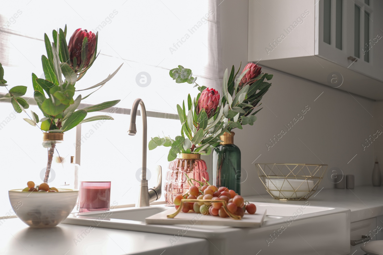 Photo of Vases with beautiful protea flowers near sink in kitchen. Interior design