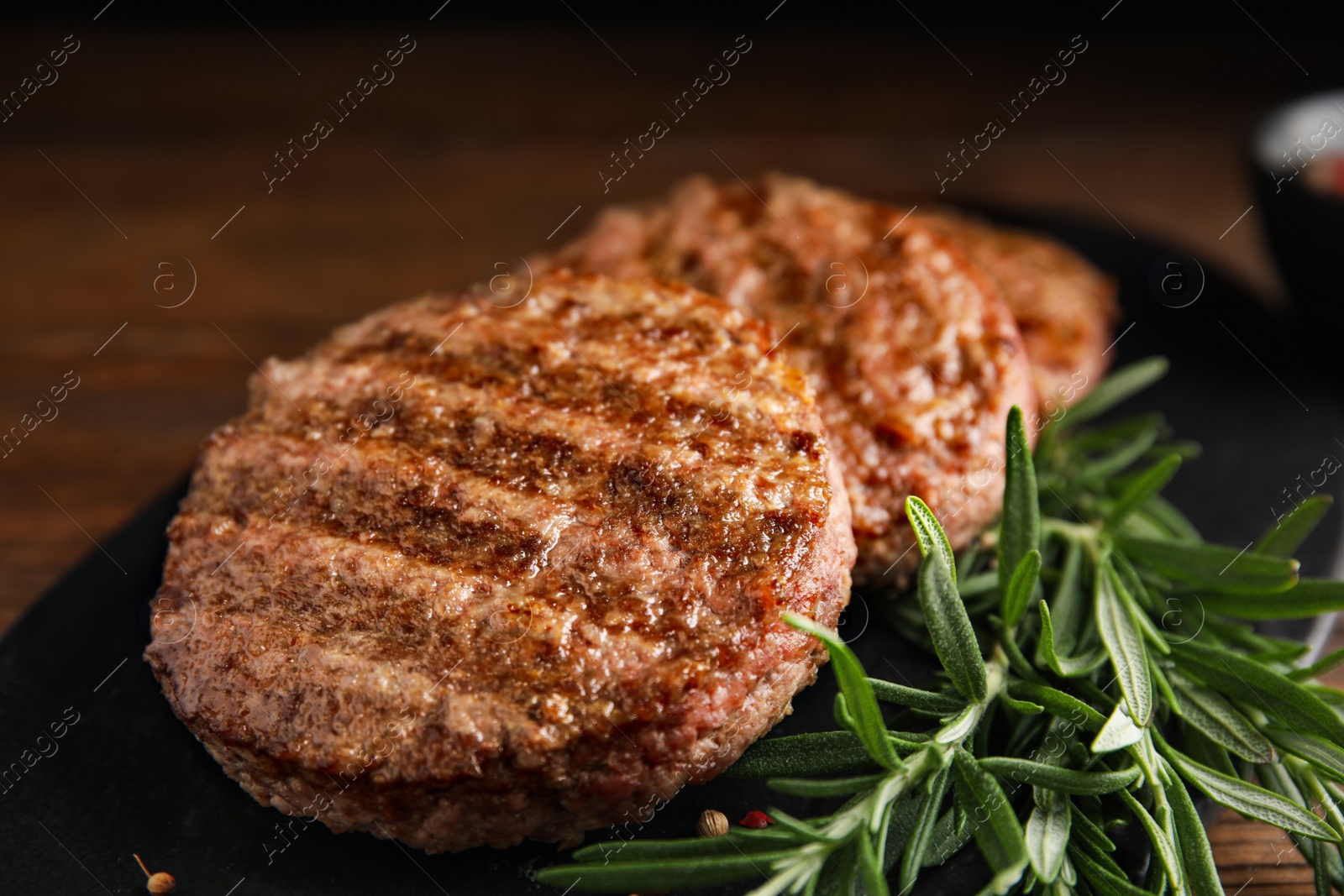 Photo of Slate plate with tasty grilled hamburger patties and seasonings on wooden table, closeup