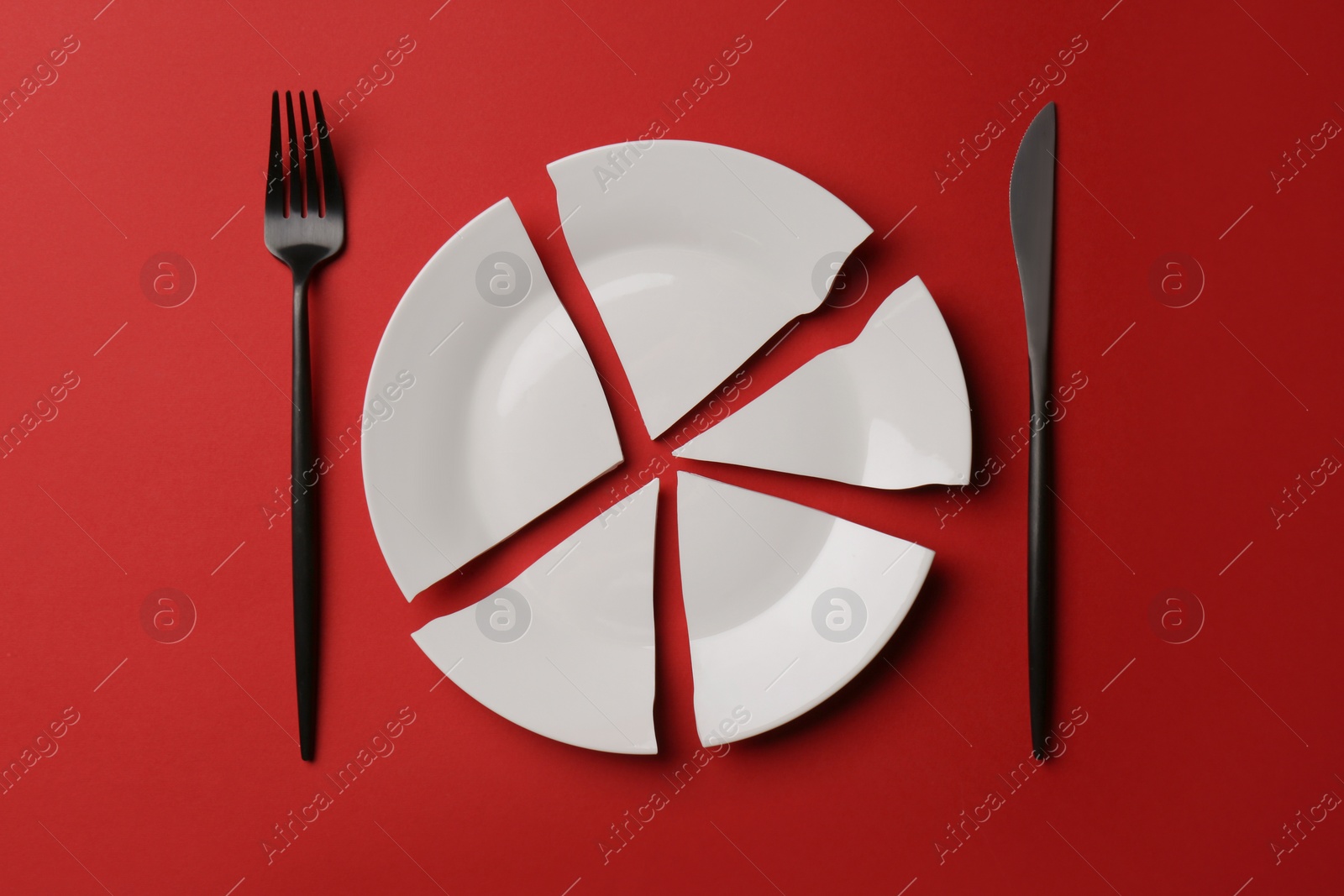 Photo of Pieces of broken ceramic plate and cutlery on red background, flat lay