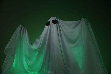 Photo of Creepy ghost. Woman covered with sheet in green light, low angle view