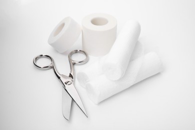 Photo of Medical bandage rolls, sticking plaster and scissors on white background
