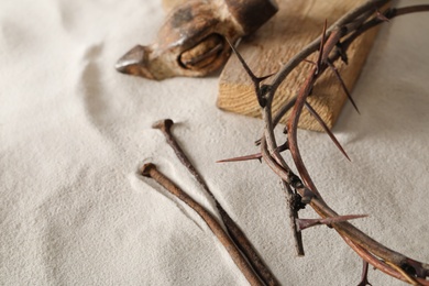 Photo of Crown of thorns, wooden plank and hammer with nails on sand. Easter attributes