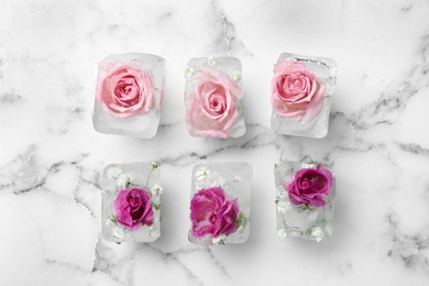 Photo of Ice cubes with roses on marble background, flat lay