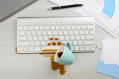 Cup of coffee spilled over computer keyboard on white office desk, flat lay