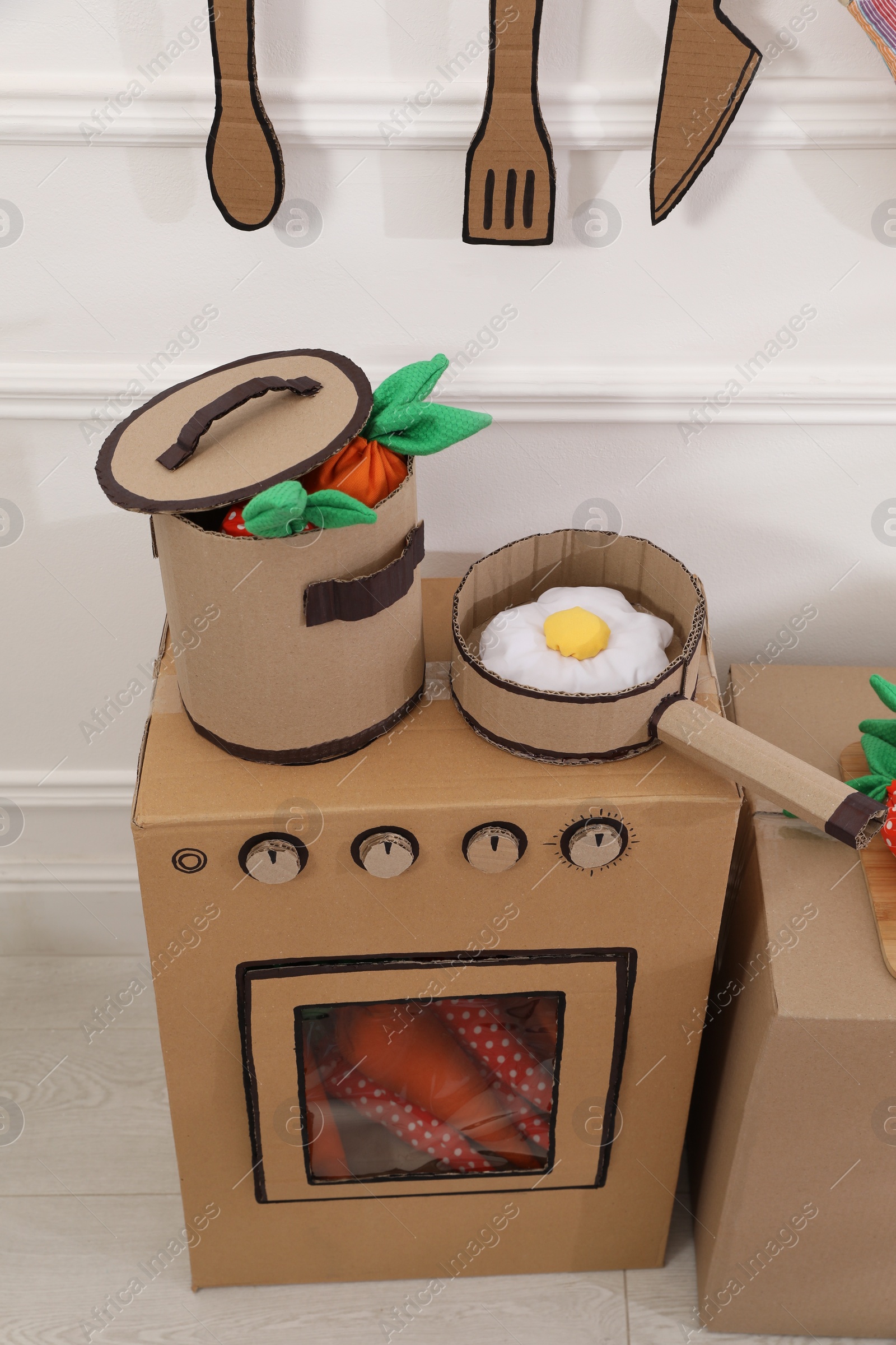 Photo of Toy cardboard kitchen with stove and utensils at home