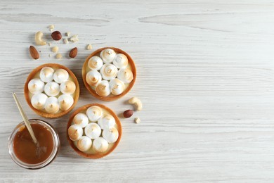Photo of Tasty dessert. Tartlets with meringue, nuts and boiled condensed milk on white wooden table, flat lay. Space for text