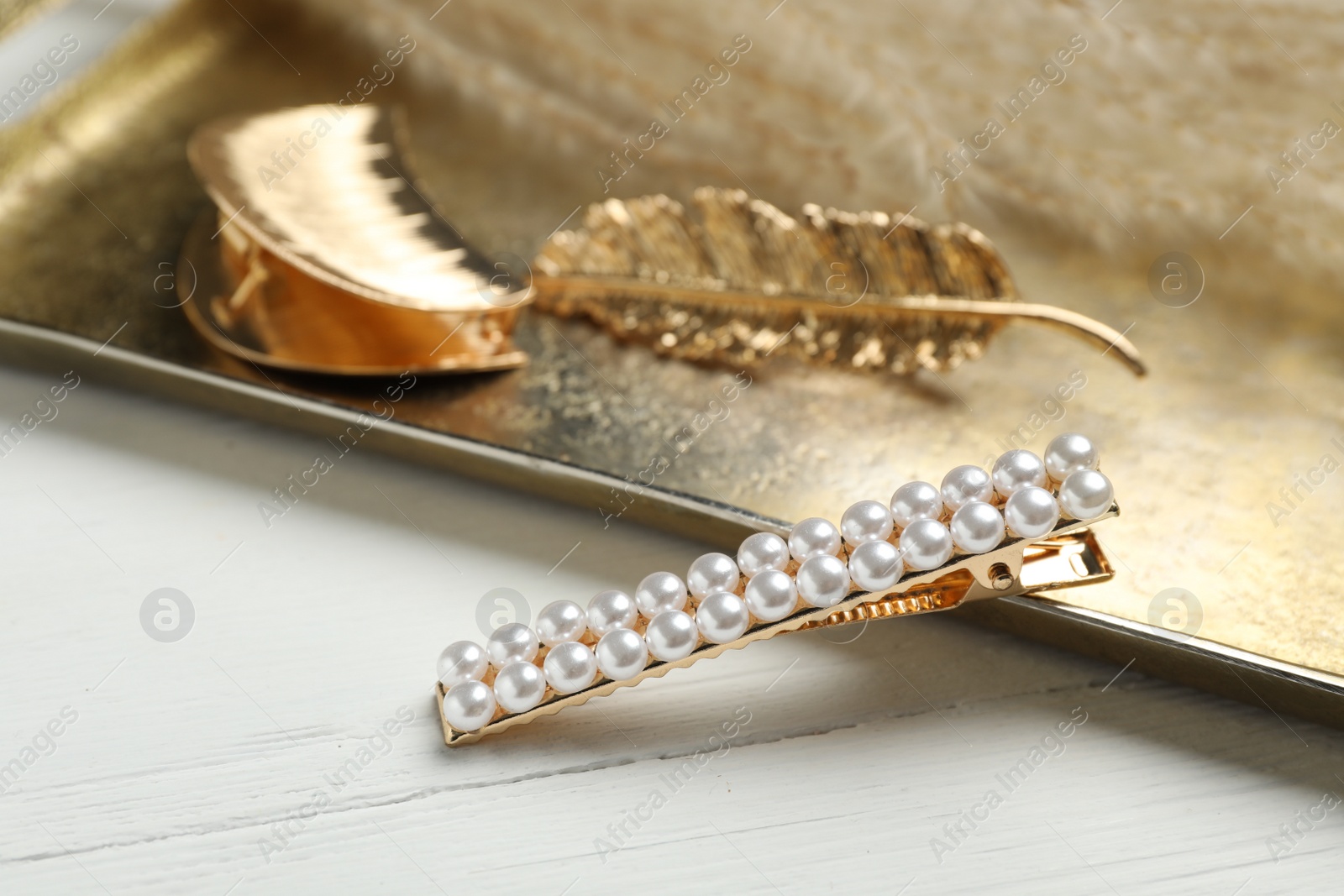 Photo of Stylish hair clips and gold tray on white wooden table