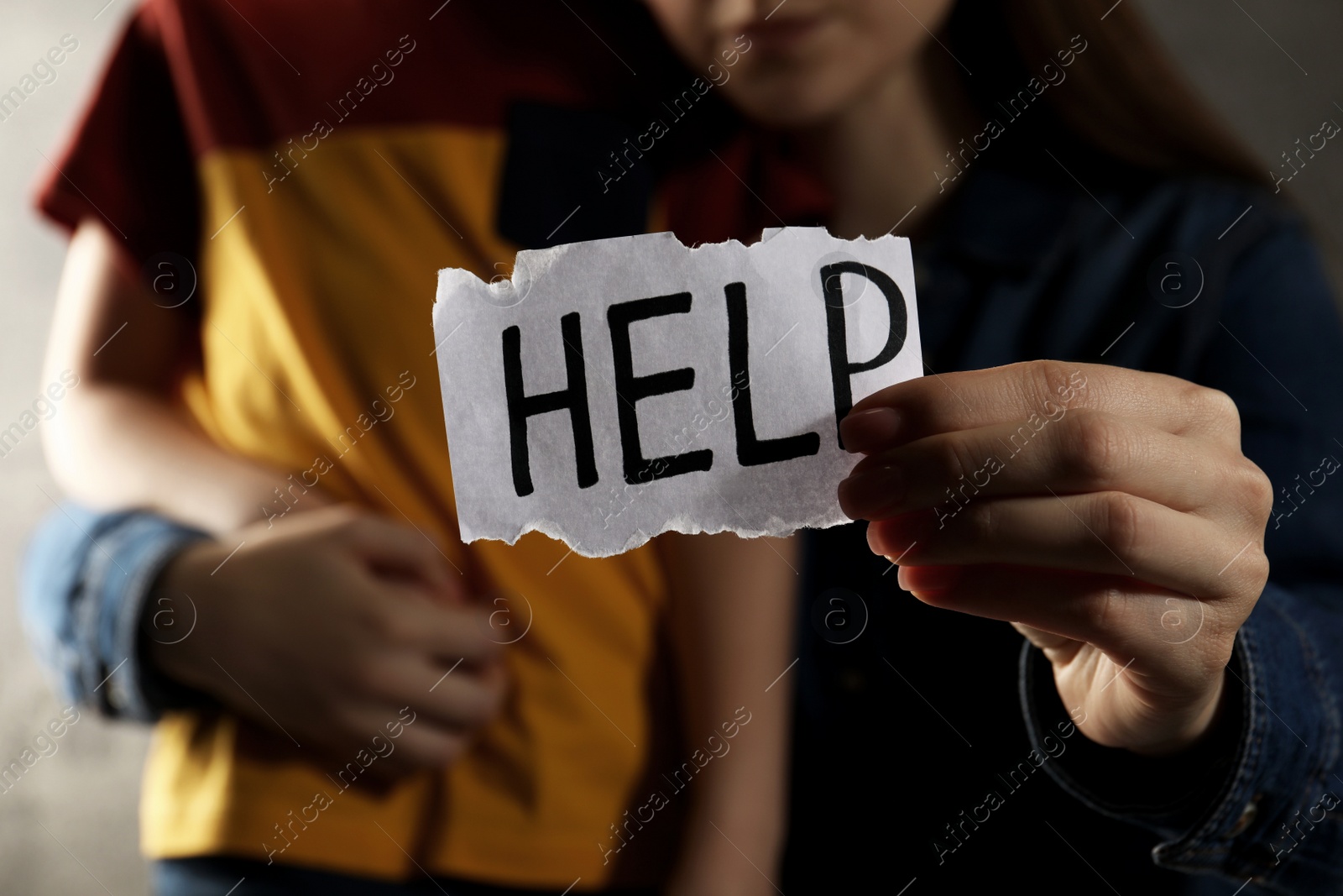 Photo of Little boy and mother holding piece of paper with word Help against light grey background, closeup. Domestic violence concept