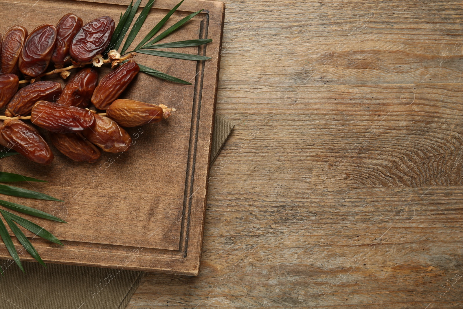 Photo of Sweet dried dates with green leaves on wooden table, top view. Space for text