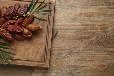 Sweet dried dates with green leaves on wooden table, top view. Space for text