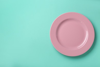 Photo of Clean pink plate on turquoise background, top view. Space for text