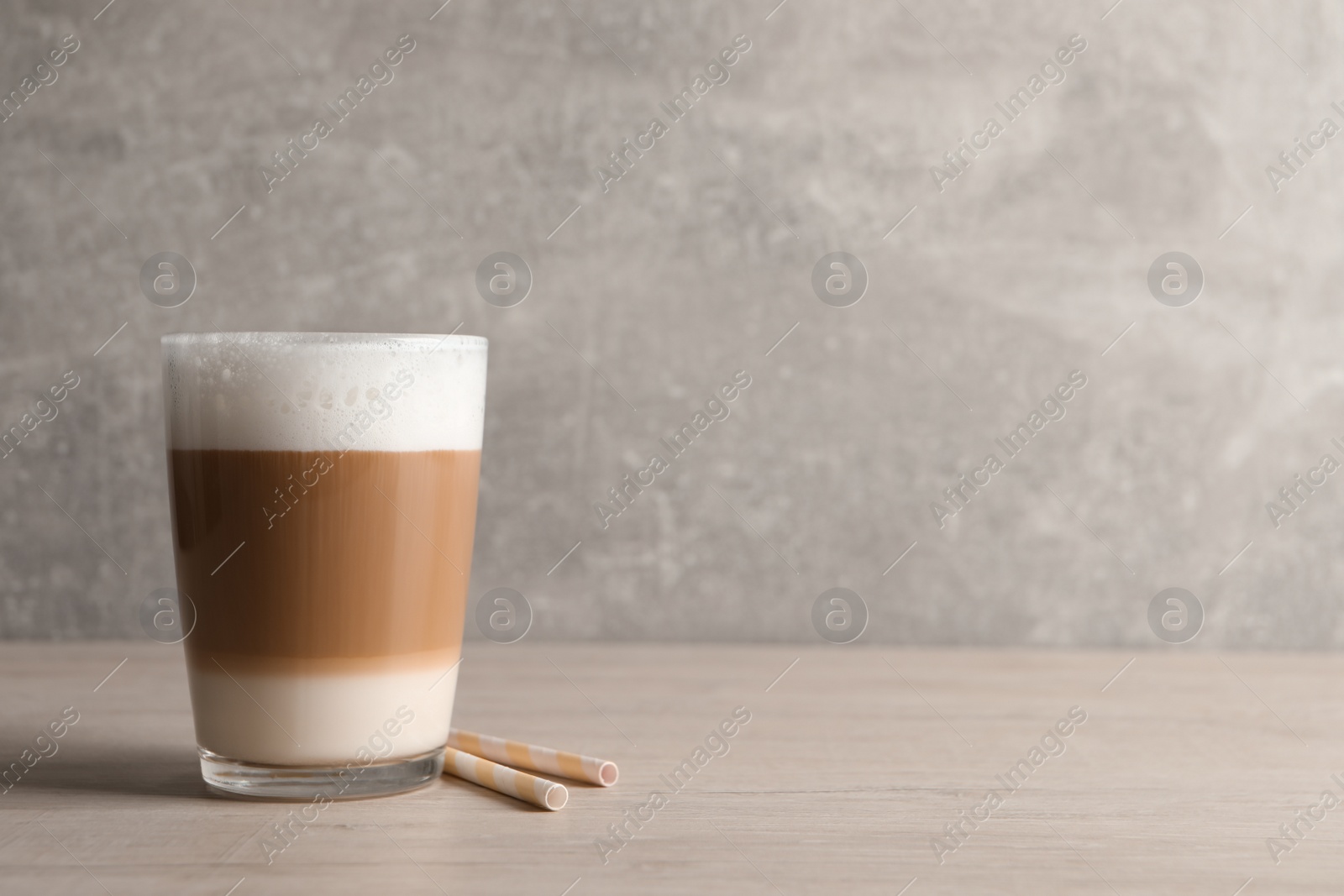 Photo of Glass of delicious layered coffee and straws on wooden table against light grey background, space for text