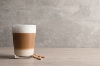 Glass of delicious layered coffee and straws on wooden table against light grey background, space for text