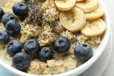 Photo of Tasty oatmeal with banana, blueberries and chia seeds served in bowl on white table, closeup