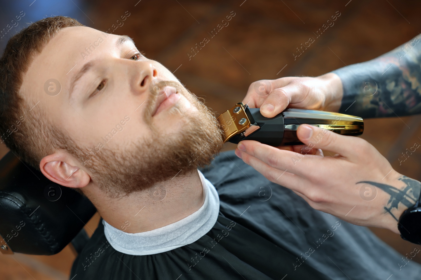 Photo of Professional hairdresser working with bearded client in barbershop, closeup