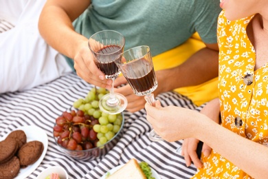 Photo of Young couple with glasses of wine having picnic outdoors, closeup