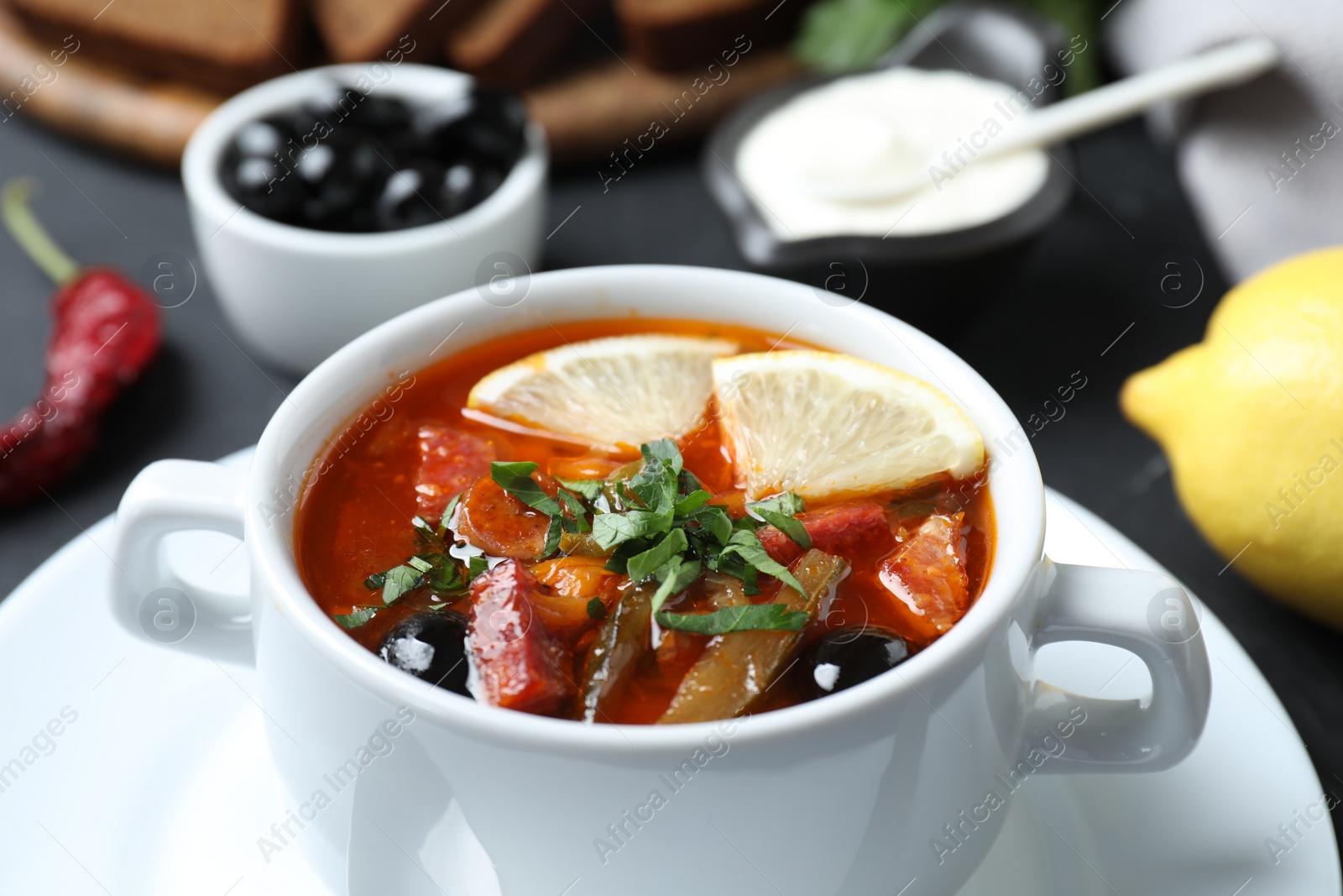 Photo of Meat solyanka soup with sausages, olives and vegetables in bowl on table, closeup