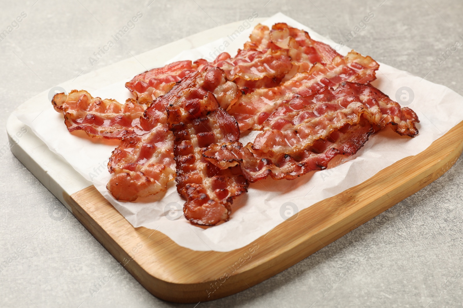 Photo of Board with fried bacon slices on grey textured table, closeup