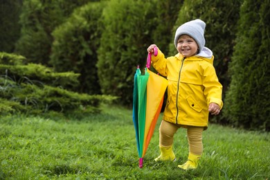 Photo of Cute little girl holding colorful umbrella and standing in garden, space for text
