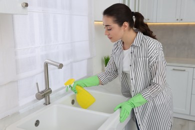 Photo of Woman with spray bottle cleaning water tap in kitchen