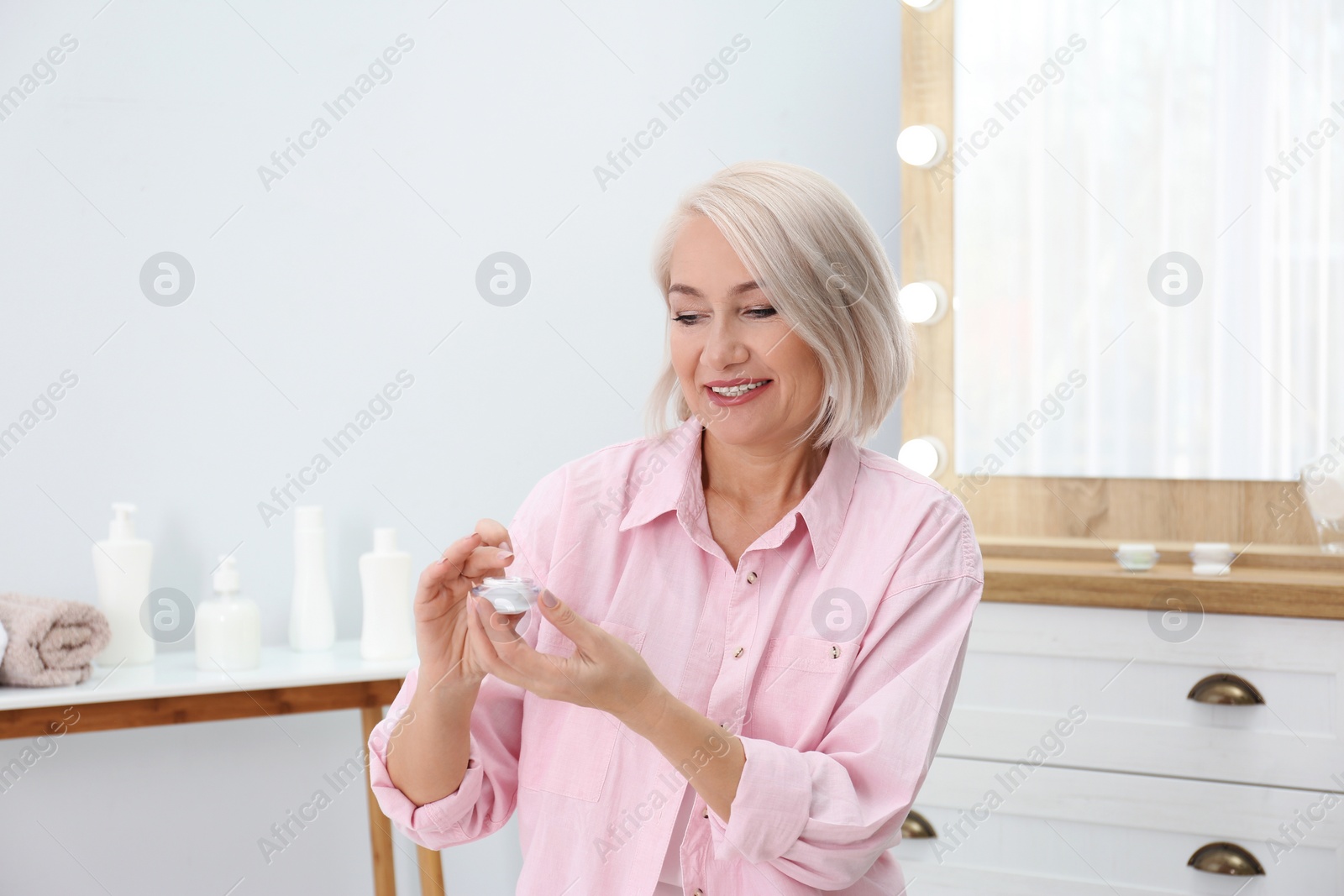 Photo of Portrait of charming mature woman with healthy beautiful face skin and natural makeup applying cream indoors