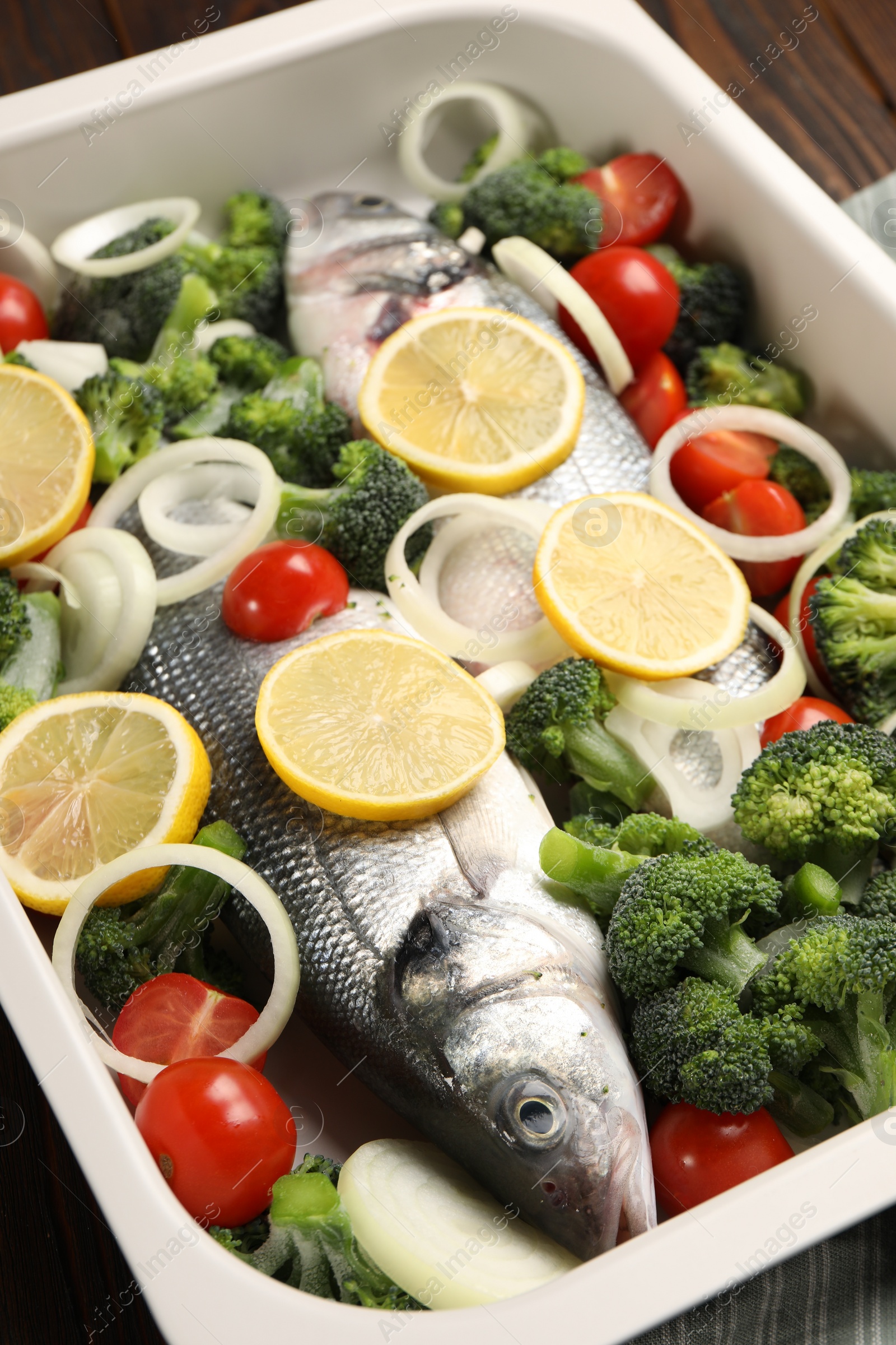 Photo of Raw fish with vegetables and lemon in baking dish on table