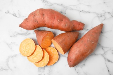Photo of Whole and cut ripe sweet potatoes on white marble table, flat lay